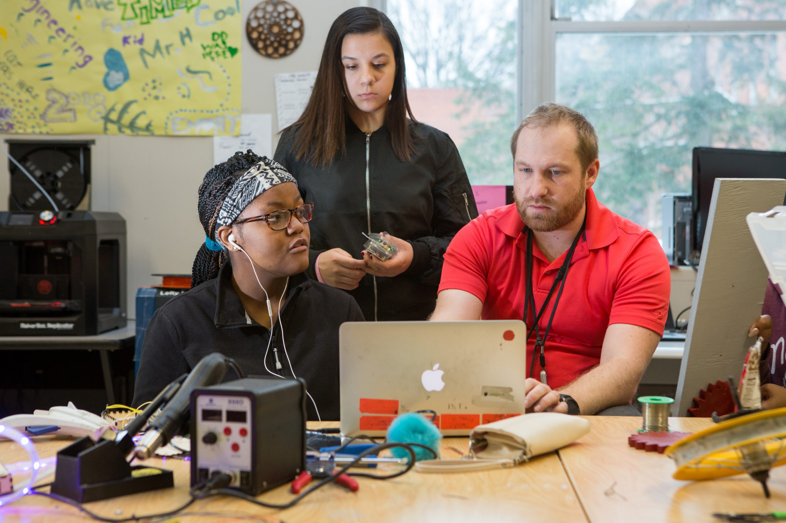 Male teacher helps two female students at computer